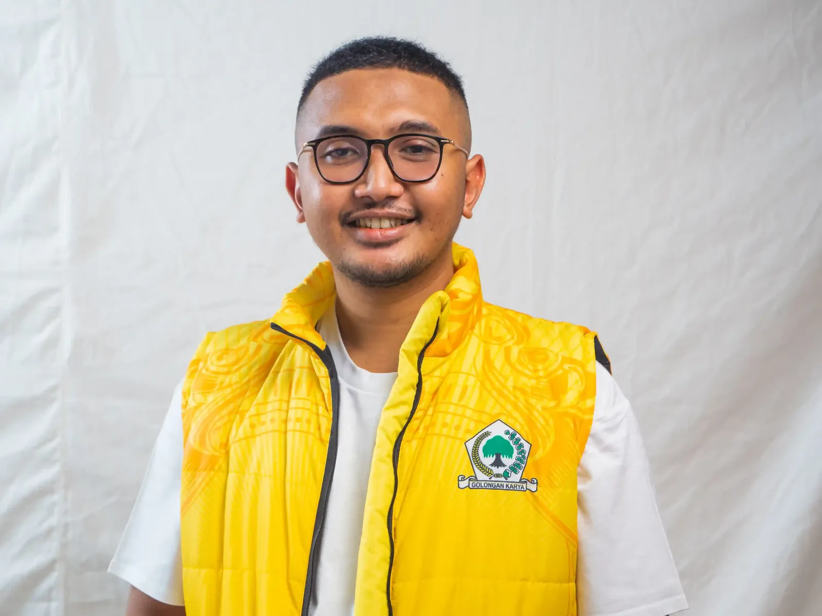 Portrait of Busfi Arusagara wearing a yellow party vest with green emblem and glasses