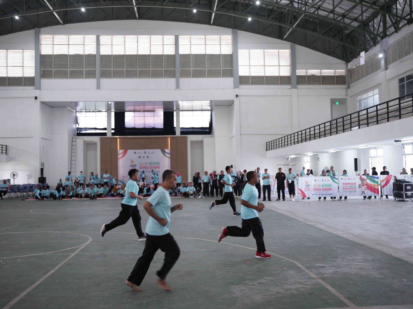 Athletes running in indoor sports venue during FORNAS VIII with event banners visible
