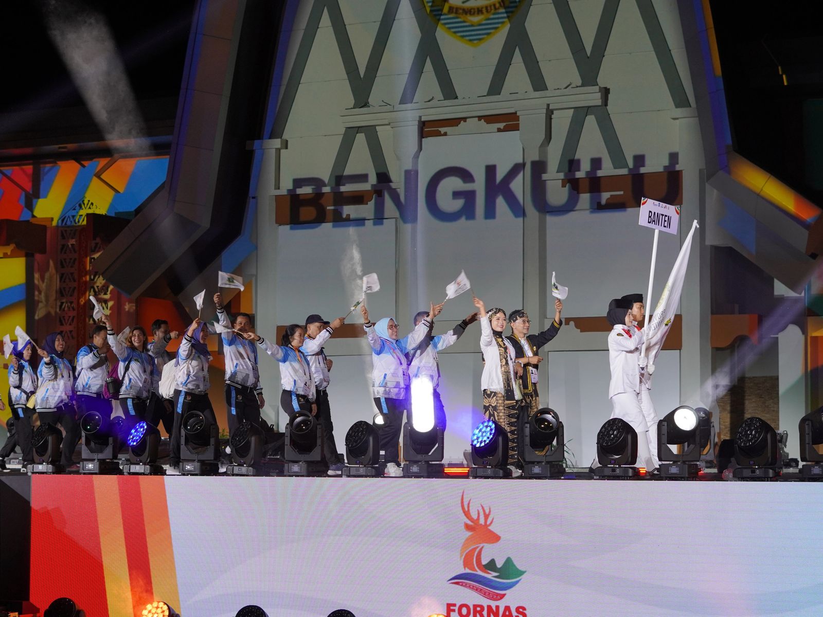 FORNAS VIII opening ceremony with performers in white uniforms holding flags on stage in Bengkulu