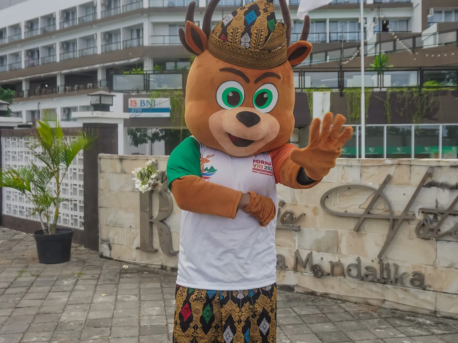 FORNAS VIII mascot deer character in traditional Indonesian clothing waving at Mandalika venue
