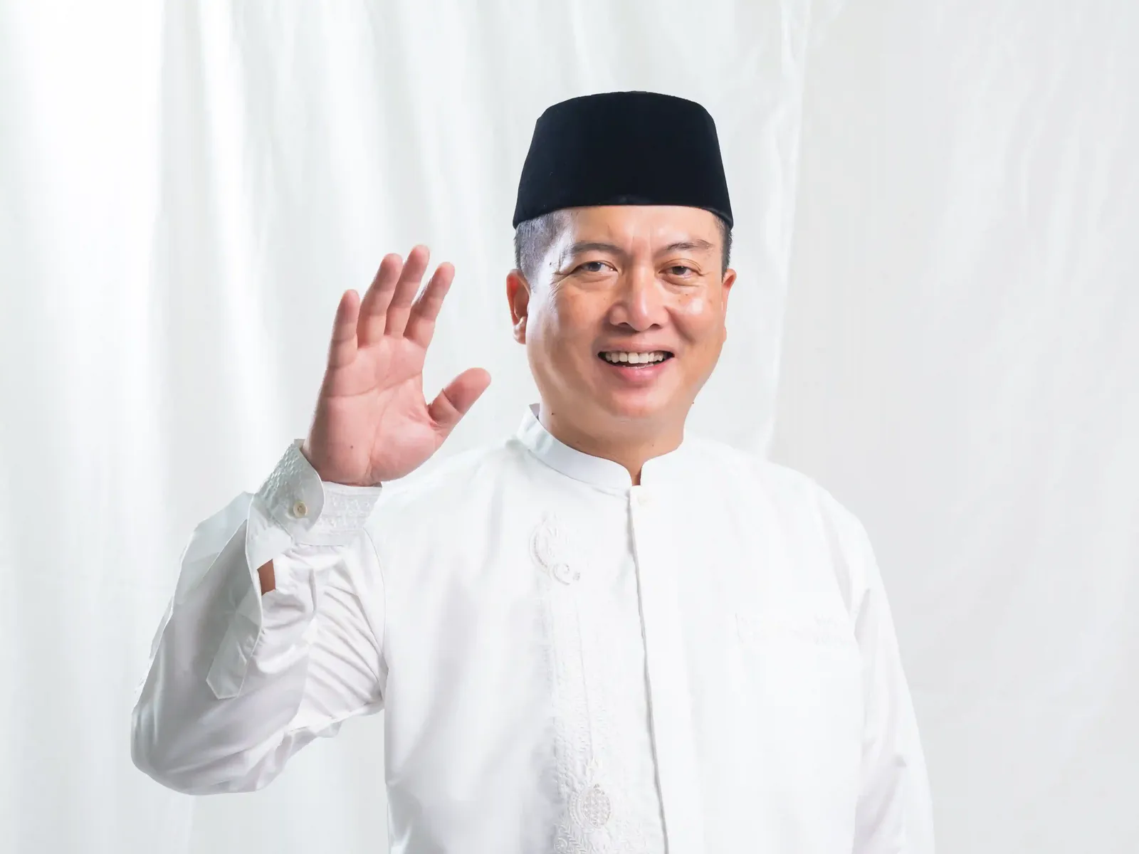 Gubernatorial candidate in traditional white clothing and black cap waving to supporters