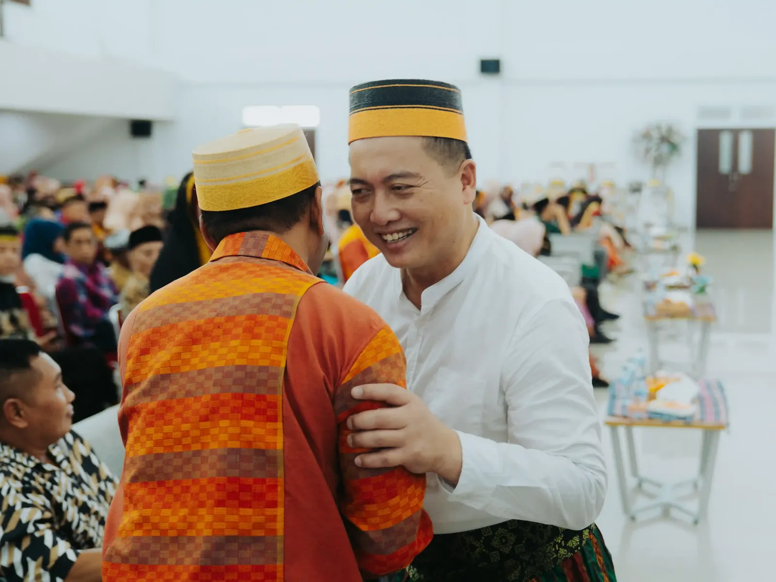 Gubernatorial candidate in white traditional clothing and yellow cap greeting a supporter in orange traditional attire