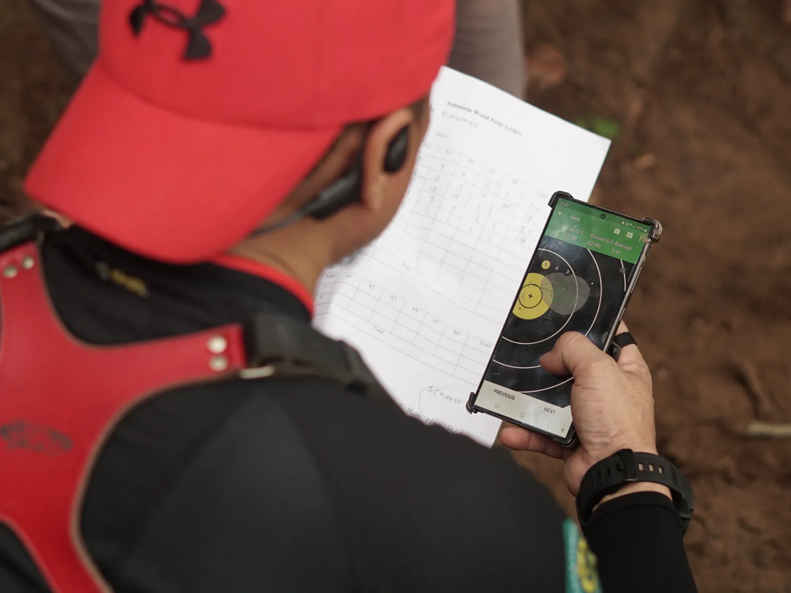 Close-up of archer's hands holding smartphone displaying archery scoring app with target diagram during competition