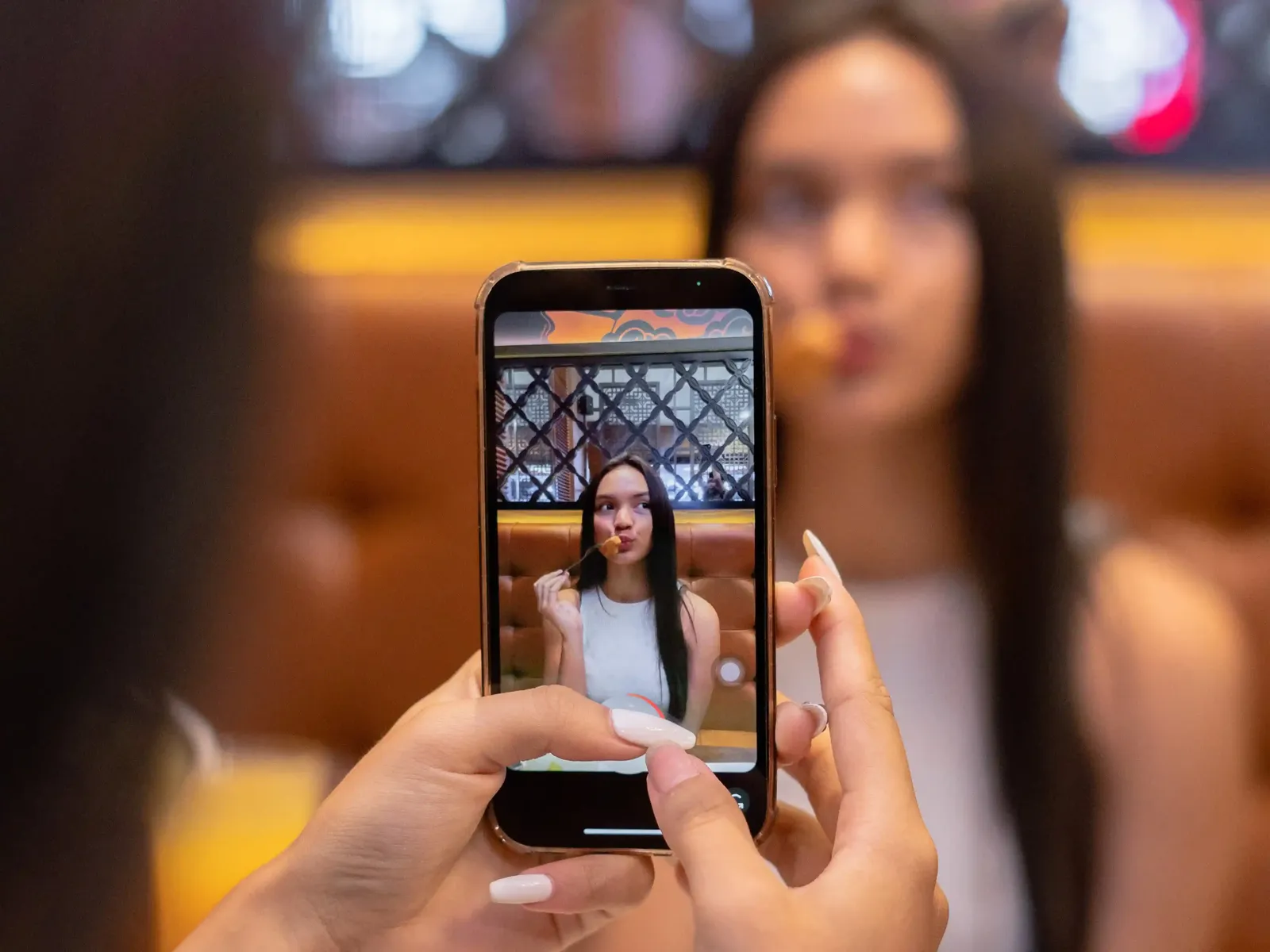 Person taking a photo of a woman eating at Resto Kenangan restaurant with decorative lattice background
